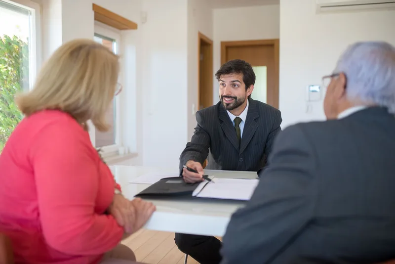 A consultant in business attire advising two clients across a desk