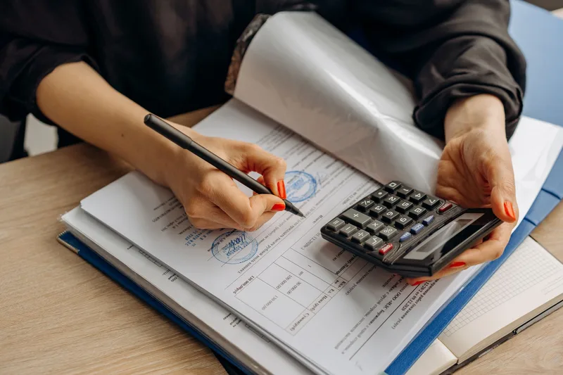 Close-up of hands using a calculator while reviewing stamped official paperwork