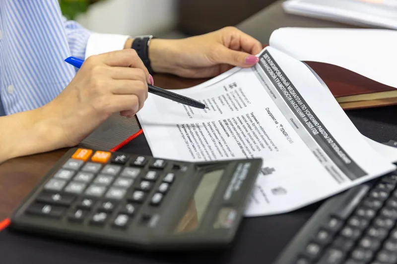 Close-up of hands reviewing a financial document with a calculator on a desk