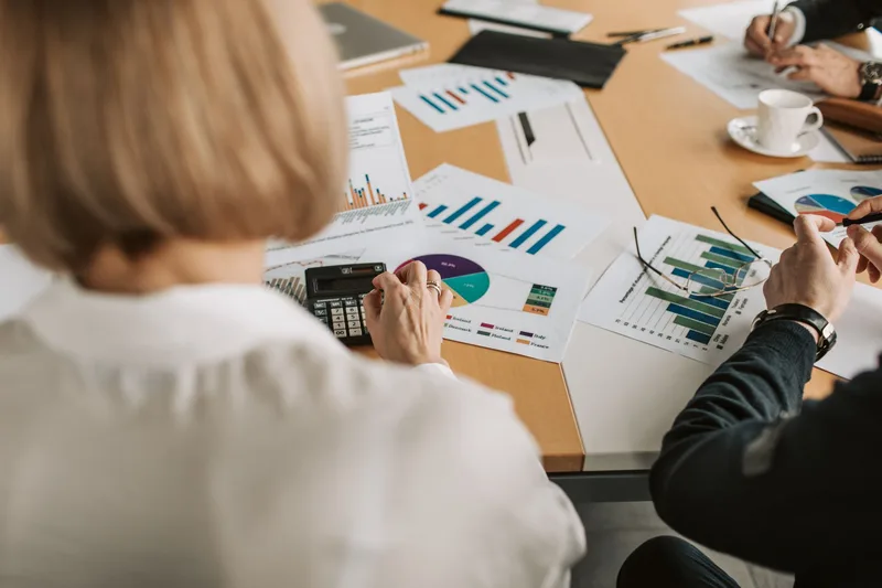 Professionals around a table reviewing printed financial charts and a calculator