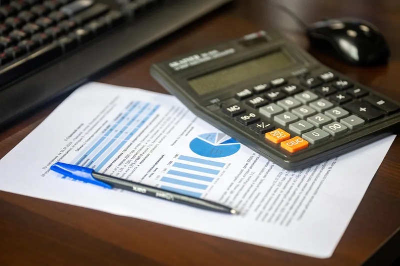 Calculator and pen resting on a printed financial report next to a keyboard
